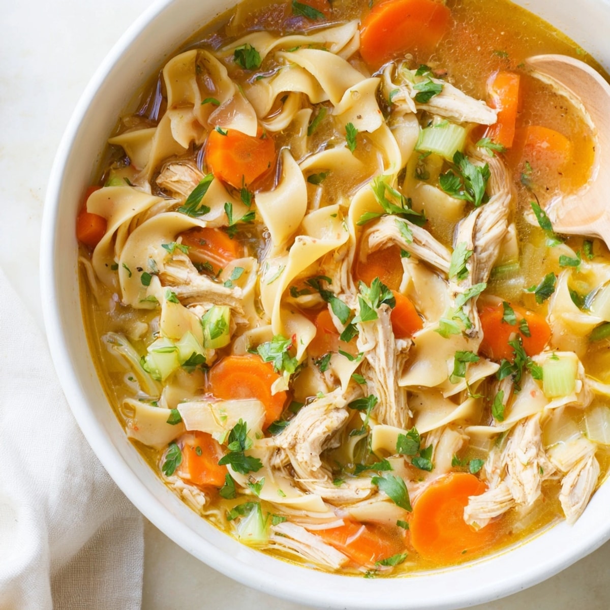 Close-up of steaming Chicken Noodle Soup with colorful vegetables and fresh parsley garnish.