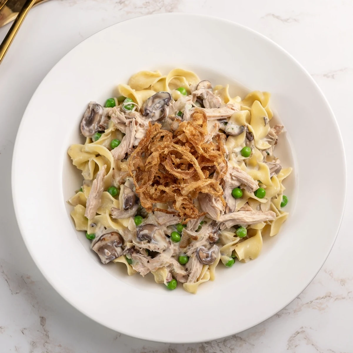 A close-up of creamy tuna noodle casserole with golden, crispy onion topping.