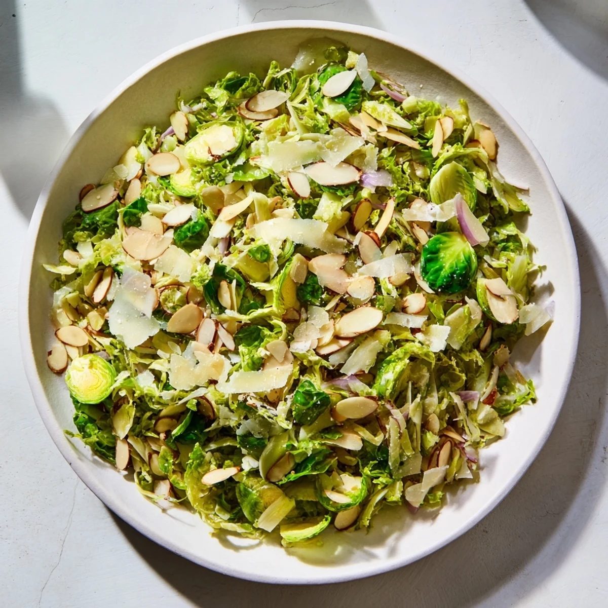 Fresh, vibrant photo of Crunchy Lemon Parmesan Brussels Sprouts Salad, topped with toasted almonds and cheese.