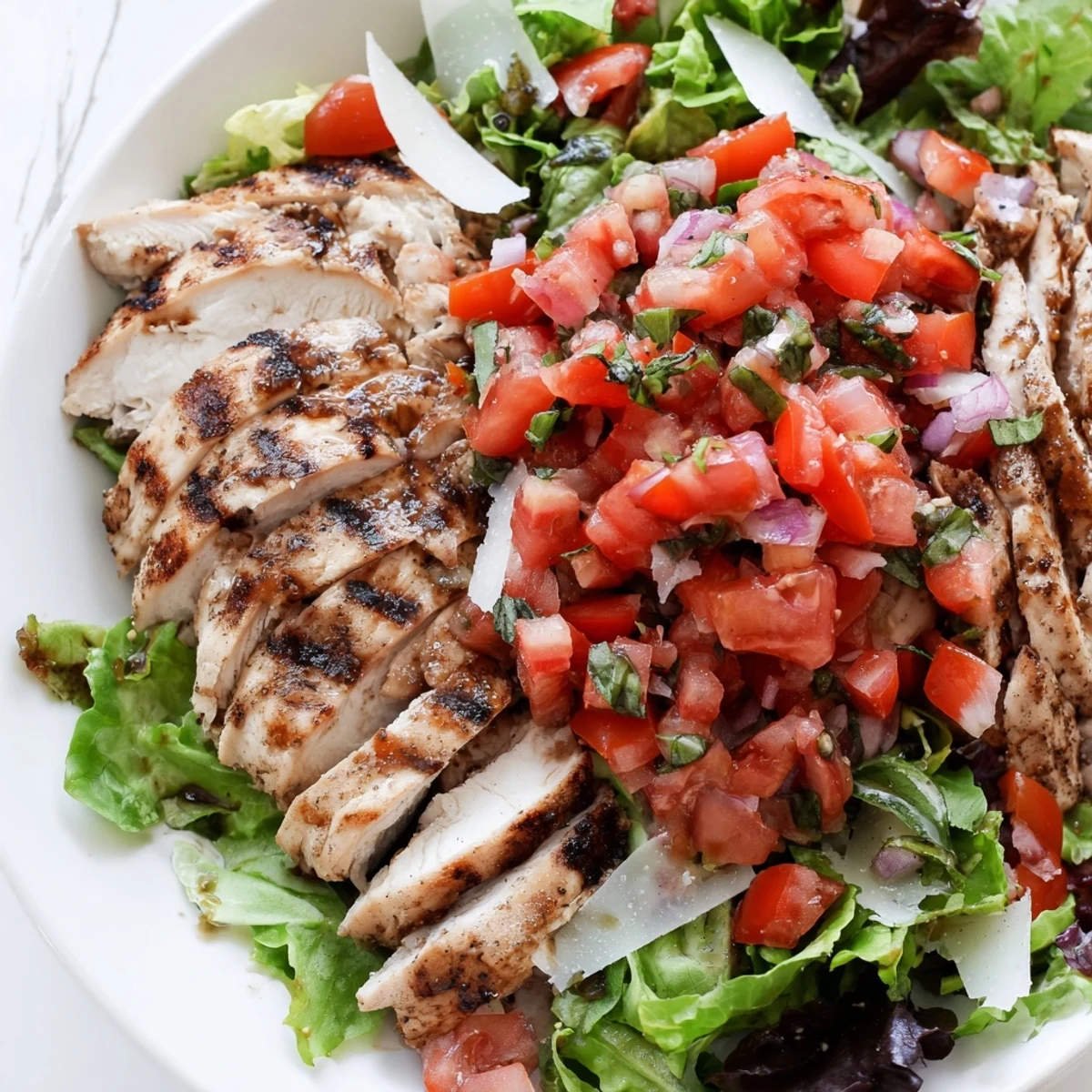 Savory Bruschetta Chicken Salad plated with lemon wedges, showcasing tender grilled chicken, balsamic tomatoes, and Parmesan over a fresh salad base.