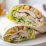 Juicy grilled chicken and crisp romaine fill a Caesar Chicken Salad Wrap on a white plate.