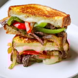 A close-up of a toasted Philly Cheesesteak Grilled Cheese, showcasing juicy steak strips, onions, and peppers tucked inside the crispy crust.