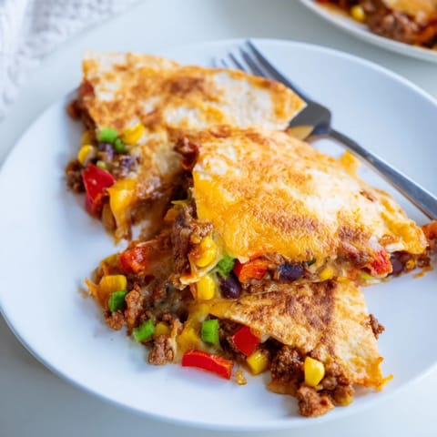 Golden-brown Sheet Pan Quesadillas with Beef, topped with vibrant veggies and cheese.  