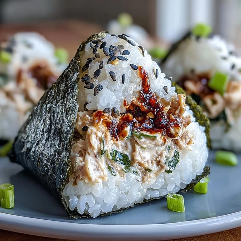 A handheld shot of homemade spicy tuna onigiri, showcasing the glossy rice and savory nori seaweed wrapping.  